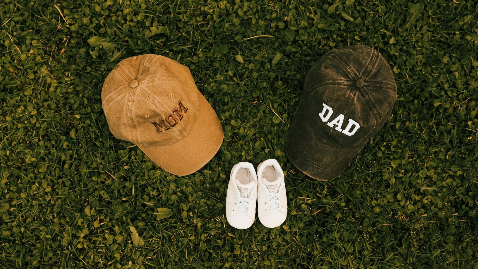 Unique family announcement concept with 'Mom', 'Dad' caps and baby shoes on grass. — How Tantric Massage Outcall in London He